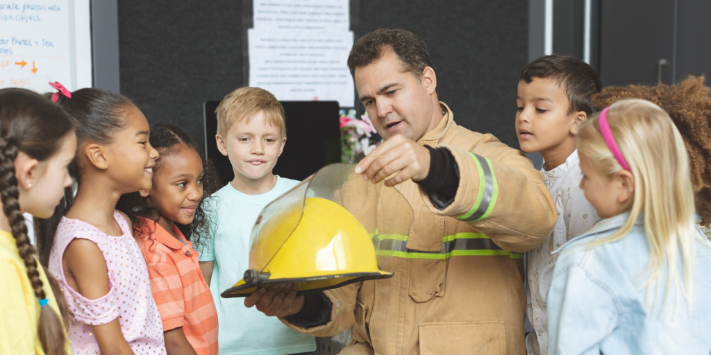 Martin is showcasing his firefighter uniform to a group of primary school children.