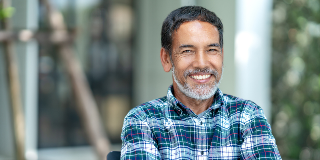 Karl is a middle-aged man with tanned skin and dark hair as well as a grey beard. He is sitting in front of a laptop in a plaid shirt and smiled confidently into the camera.