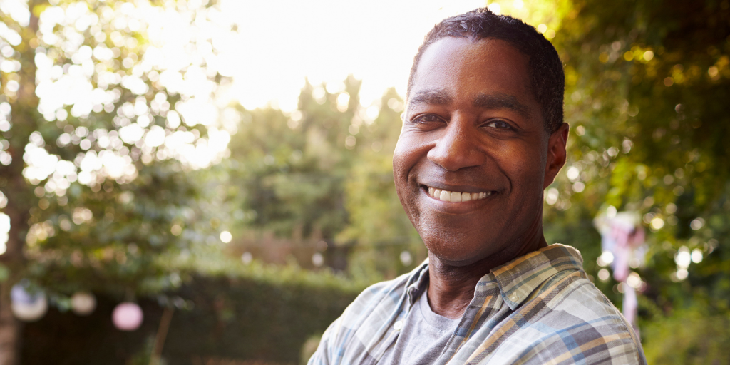 Hilbert is a black man in his 50s. He has a wide smile and is standing outside in his garden.